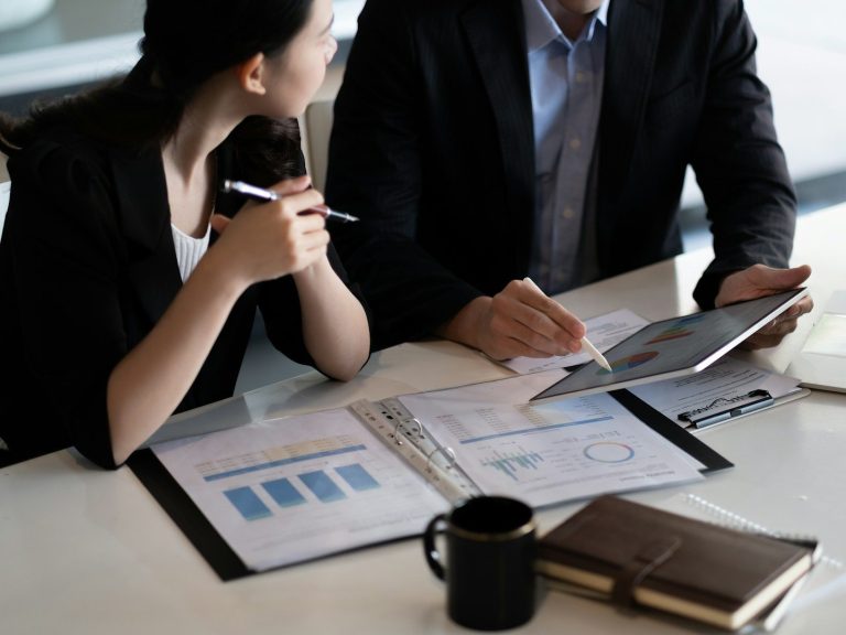 Beratungsgespräch Zwei Personen diskutieren über Diagramme und Daten auf einem Tisch.