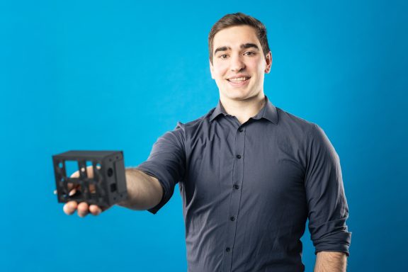 Ein Mann hält ein schwarzes Modell in der Hand, vor einem blauen Hintergrund.