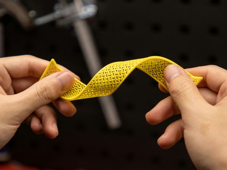 Eine Person hält ein gelbes, gewundenes Stück Material zwischen den Händen und tordiert es.